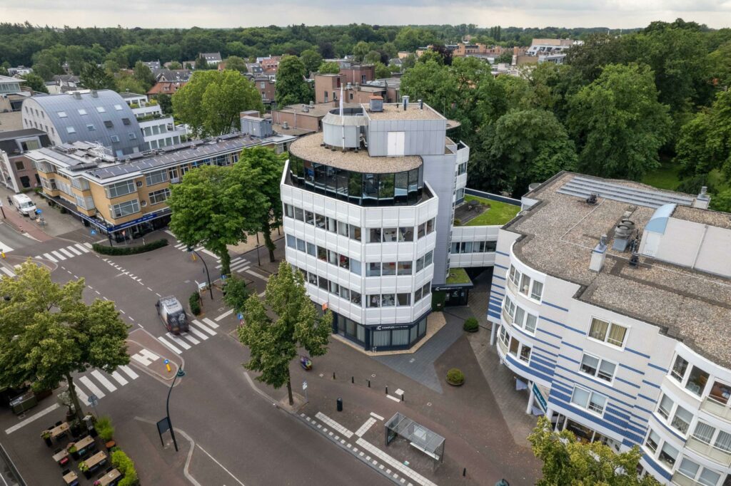 Luchtfoto van het kantoorgebouw aan de 1e Hogeweg, gelegen op een kruispunt in een groene stedelijke omgeving.